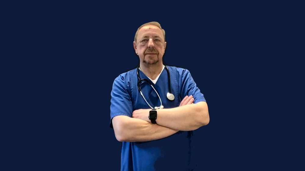 Michael Bethke in Pflegekleidung mit Stethoskop, mit verschränkten Armen